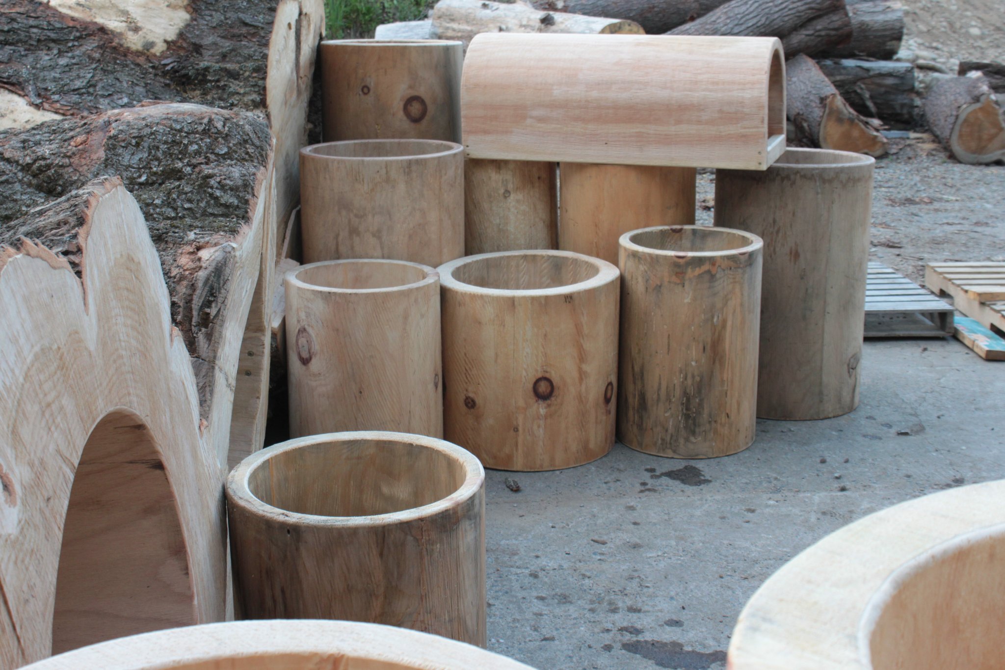 IC WOOD production yard full of finished bark-free hollow cylinders in every size, half-log pieces, tunnel section on top, raw logs in background — the complete product lineup
